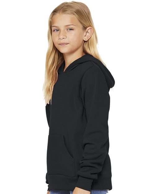 A young girl with long blonde hair is wearing a BELLA + CANVAS Youth Sponge Fleece Hoodie, made from soft Airlume combed cotton, with her hands in the front pocket. She slightly faces to the side against a plain white background.