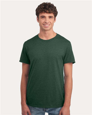 A person wearing a dark green JERZEES - Premium Blend Ring-Spun T-Shirt and jeans smiles against a plain light background. They have curly hair and a relaxed posture.