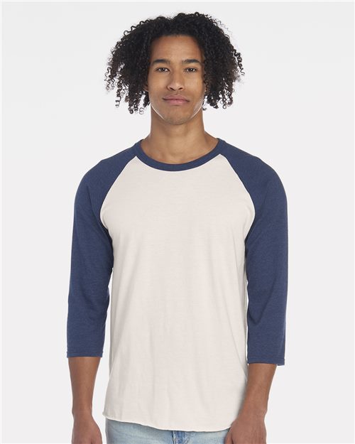 Load image into Gallery viewer, A man with curly hair is wearing a JERZEES Premium Blend Ringspun Three-Quarter Sleeve Raglan Baseball T-Shirt with blue sleeves, standing against a plain white background.
