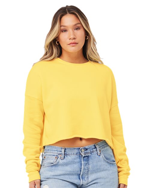 A person with long hair is wearing BELLA + CANVAS Women's Crop Crew Fleece in bright yellow, paired with light blue jeans. They have a neutral expression and stand against a plain background.