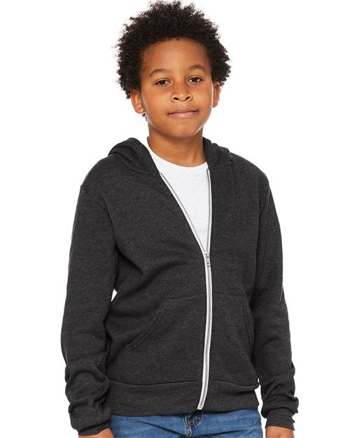 A curly-haired boy wears a BELLA + CANVAS Youth Sponge Fleece Full-Zip Hoodie over a white Airlume combed cotton T-shirt and unisex blue jeans, facing forward against a plain white background.