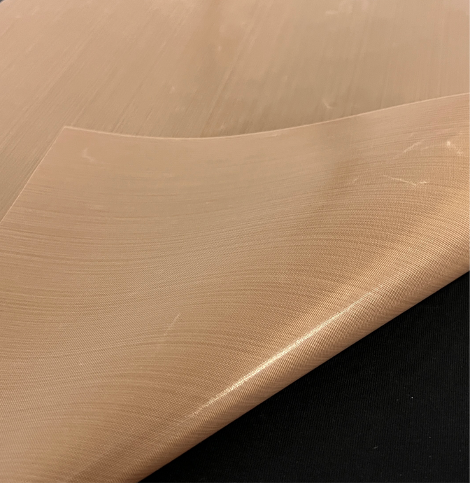 Close-up of a partially folded beige Teflon Sheet (16x20”) by Quick Transfers, showcasing its glossy surface and flexible, smooth texture on a dark background, much like fiberglass fabric known for exceptional heat distribution.