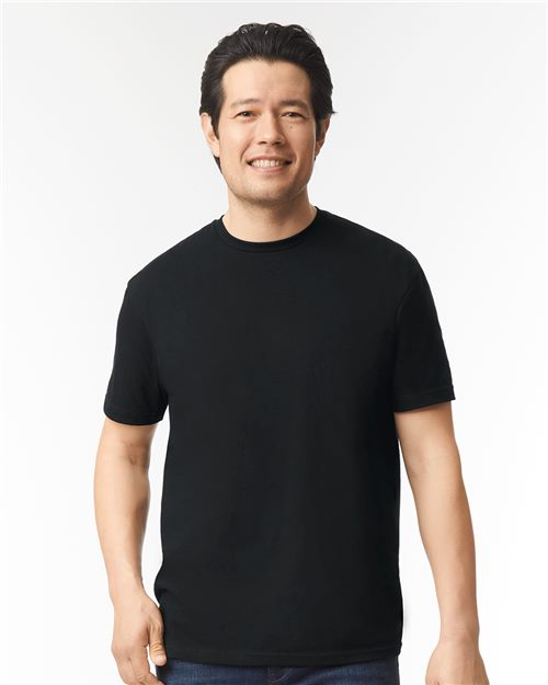 Load image into Gallery viewer, A person wearing a Gildan - Softstyle® CVC T-Shirt in black and blue jeans stands against a plain white background, smiling.
