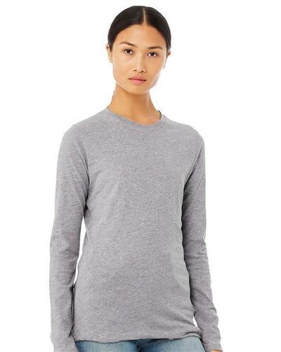 A person with long dark hair tied back is wearing a BELLA + CANVAS Women's Jersey Long Sleeve Tee in gray and semi-relaxed fit light blue jeans. They stand against a plain white background, exuding effortless style and comfort.