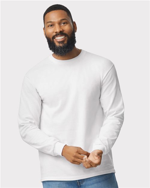 Load image into Gallery viewer, A bearded man smiles in a Gildan - Heavy Cotton™ Long Sleeve T-Shirt paired with blue jeans, set against a plain light gray background, exuding confident high-visibility standards.
