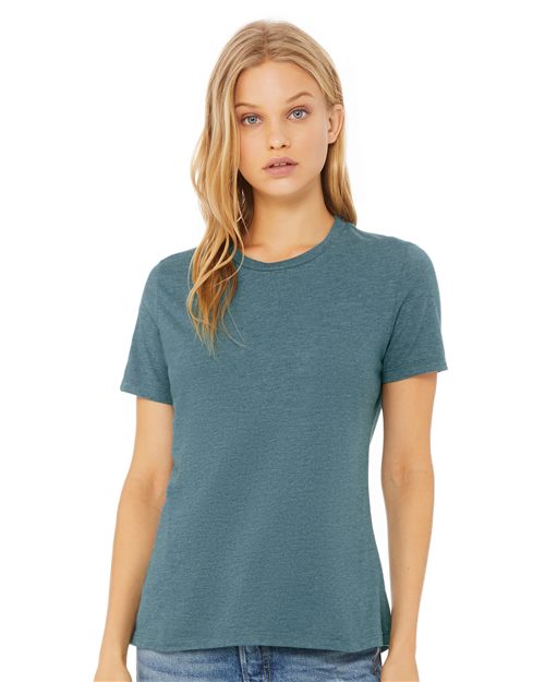 A person with long blonde hair is wearing a teal BELLA + CANVAS Women’s Relaxed Fit Heather CVC Tee and blue jeans, standing against a plain white background.