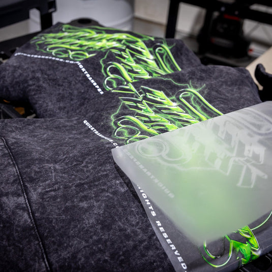 A black garment on a heat press features a neon green and white graphic design from Quick Transfers' FASTFILM™ DTF TRANSFERS, with "Cultural Atrocity" and "All Rights Reserved" prominently displayed in high-quality customized transfers near the shirt's edge.