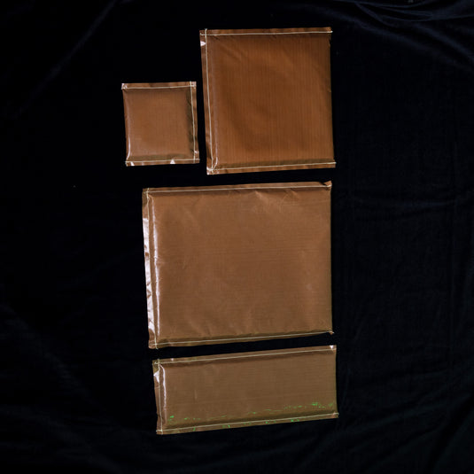 Four brown-paper-wrapped packages on a dark background include the Quick Transfers Press Pillows (4 Pack) for heat pressing. The packages vary in size: one small, one medium, one large square, and one large rectangle.